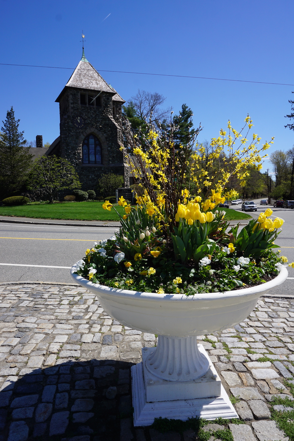 Watering trough with yellow flowers with First Parish Church in background on clear sunny day.