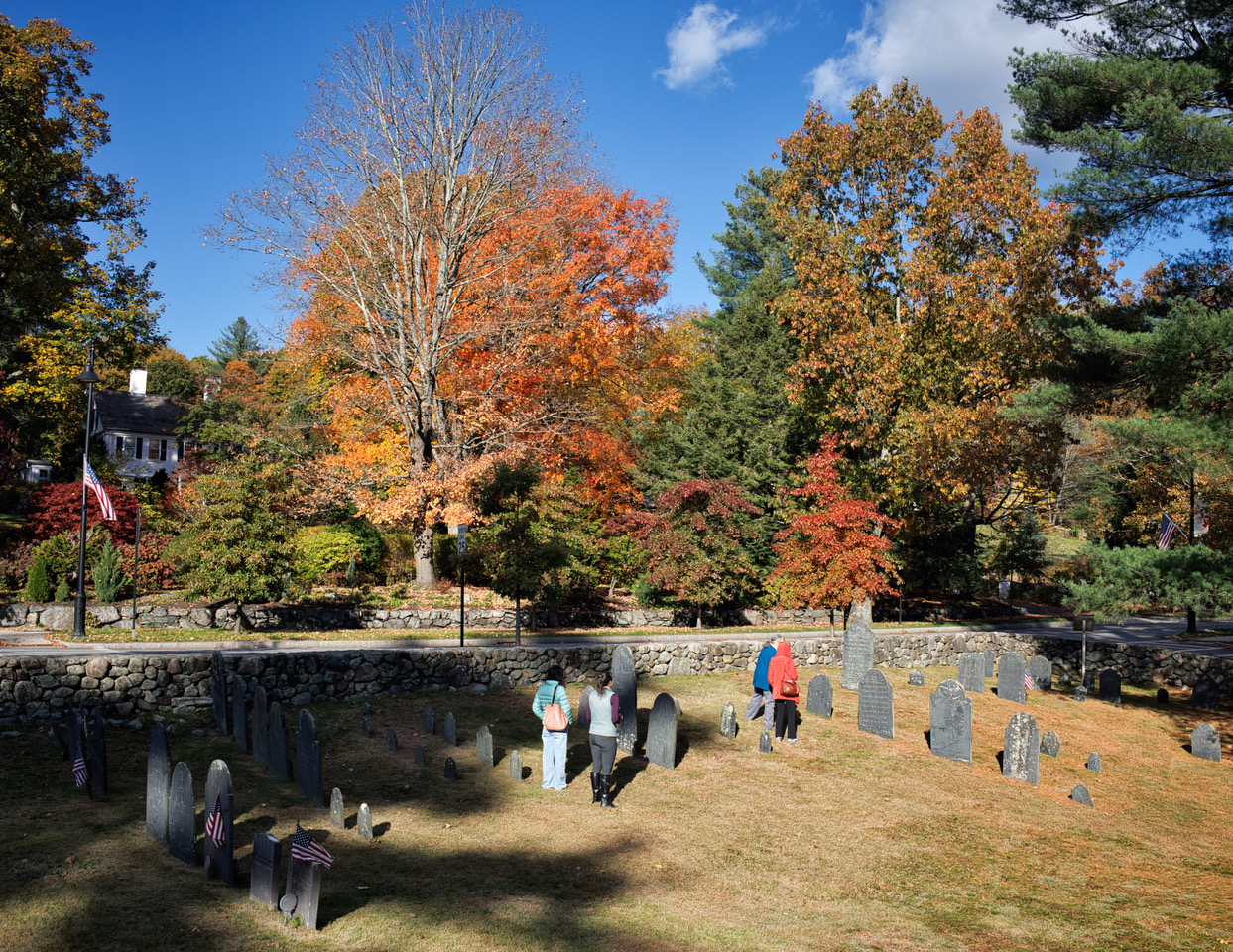 Elevated view of attendees viewing graves in Farmers' Burial Ground, with maples with bright fall foliage across the Post Road beyond.